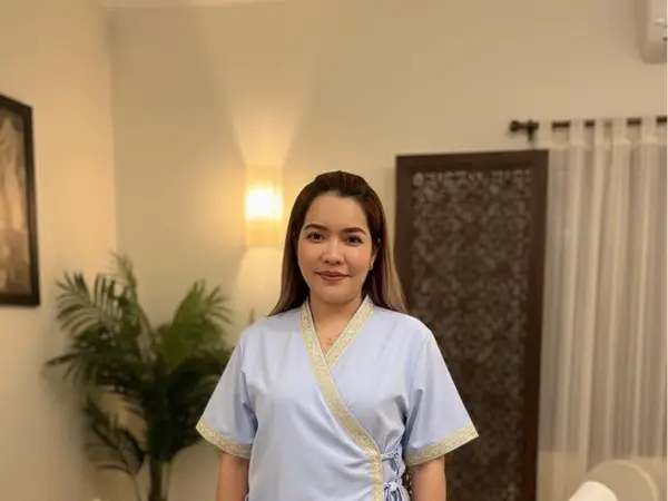 Thai massage room with a woman in blue uniform, plant, lamp, and curtain divider