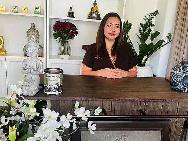 Thai massage reception with a woman behind a wooden desk, plants, and Buddha decor