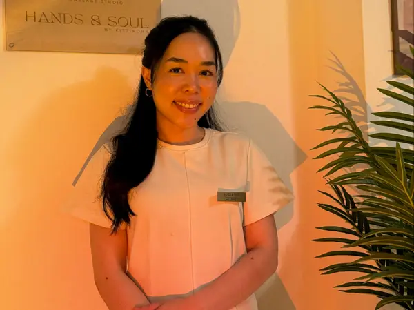 Warm-lit salon interior with a smiling woman in white beside a plant