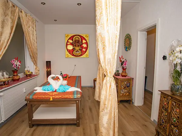 Thai massage room with a treatment table, gold curtains, and ornate decor