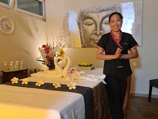Warm massage room with flower-decorated table and smiling therapist standing beside it
