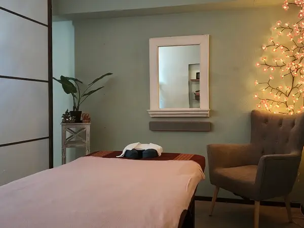 Cozy massage room with bed, chair, mirror, and soft decorative lights