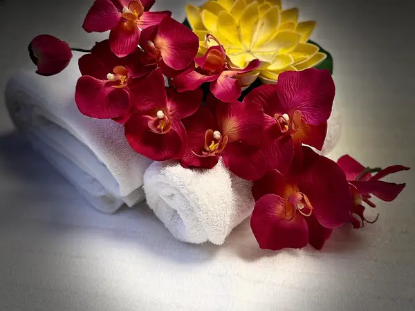 Rolled white towels with red and yellow orchids on a spa table