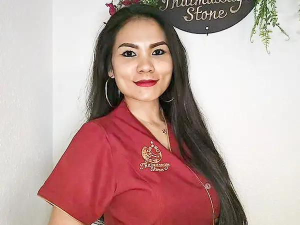 Woman in red uniform standing beside a Thaimassage Stone sign