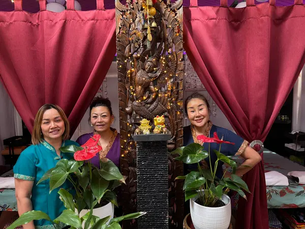 Three women pose in a decorated Thai massage room with red curtains and plants