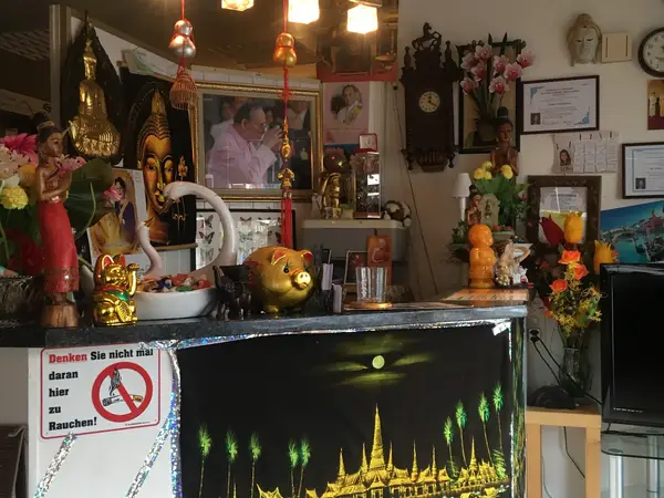 Decorated Thai massage reception with ornate statues, flowers, framed certificates, and warm lighting