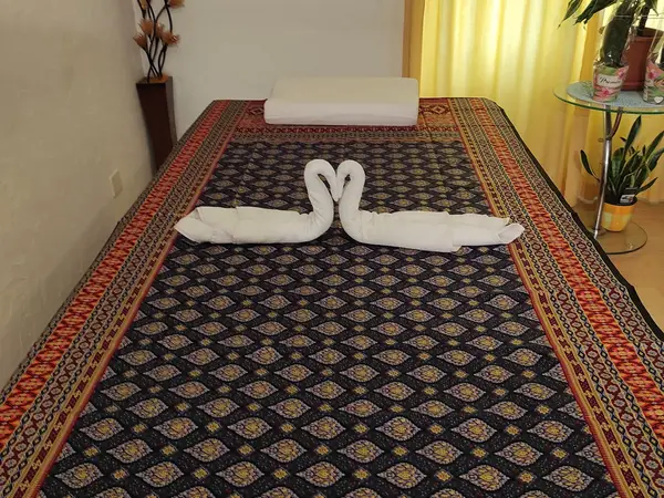 Massage room with patterned mat, folded towels, cushion, and potted plants