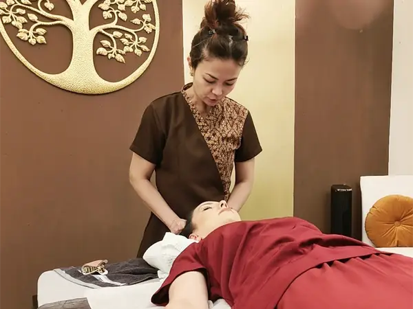 Thai massage room with therapist treating a reclining client, warm brown decor