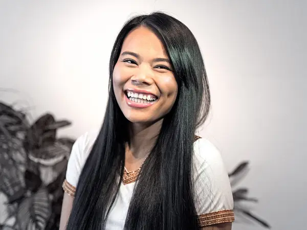 Smiling woman indoors with long black hair and plants in background