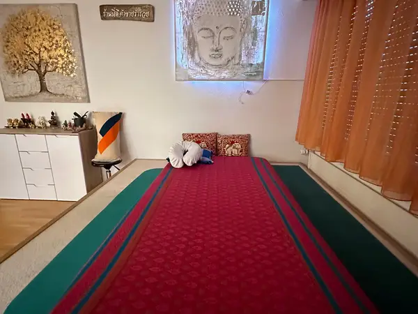 Thai massage room with mat, Buddha art, orange curtains, and decorative cabinet