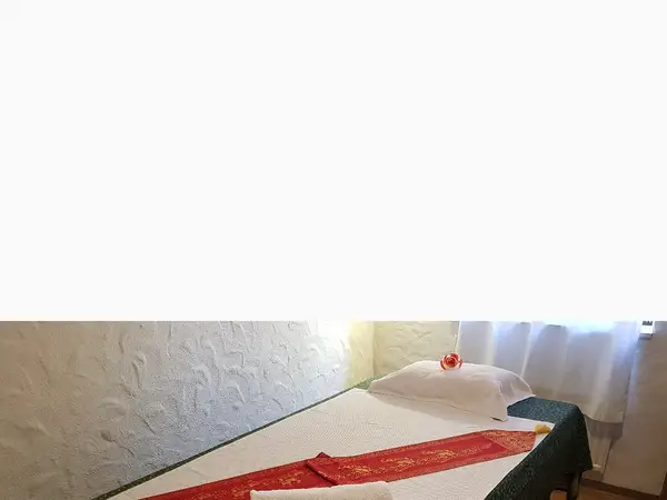 Massage table with white linens, red runner, and a small flower by curtained window