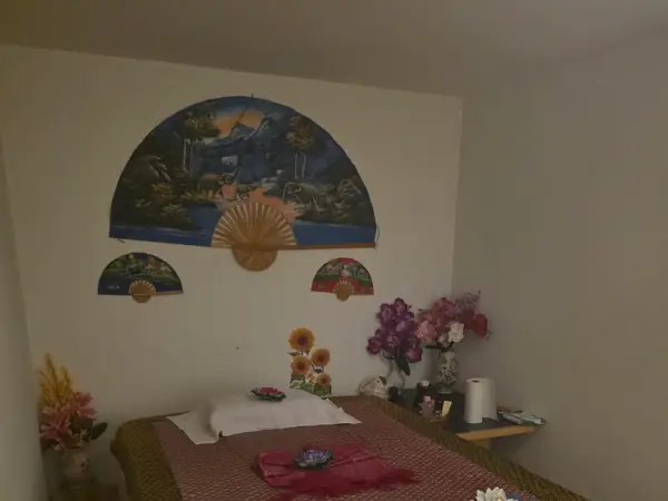 Dim massage room with bed, wall fans, and floral decor