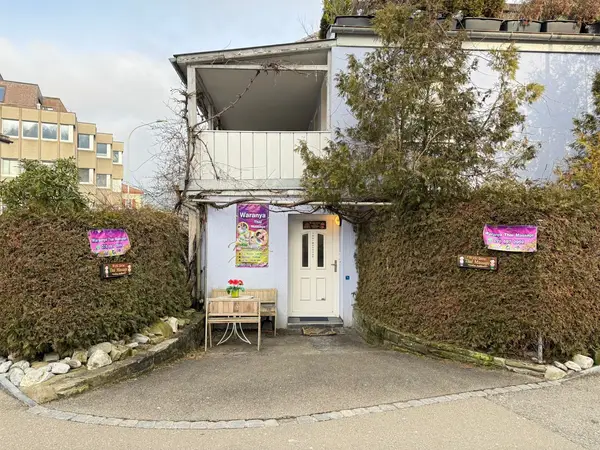 Exterior of a white house entrance with hedge-lined path and Thai massage signs