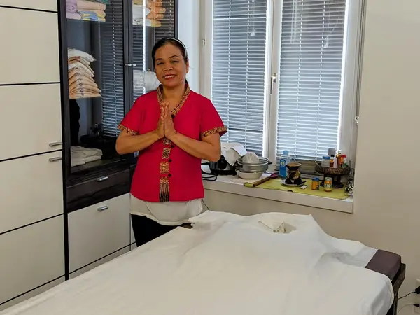 Massage room with treatment bed, cabinets, and a smiling therapist in red