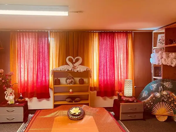 Cozy massage room with red curtains, warm decor, and a treatment bed