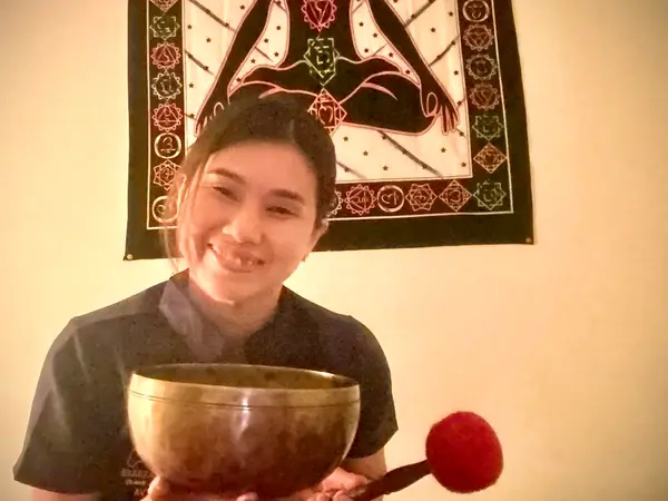 Smiling woman holding a singing bowl in a warmly lit treatment room