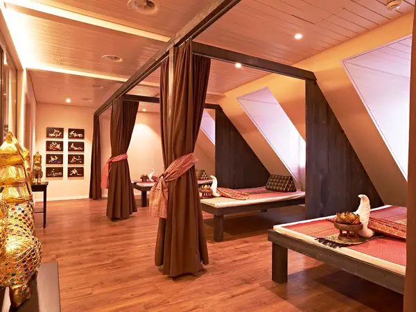 Warm Thai massage room with curtained beds, wooden floors, and decorative accents