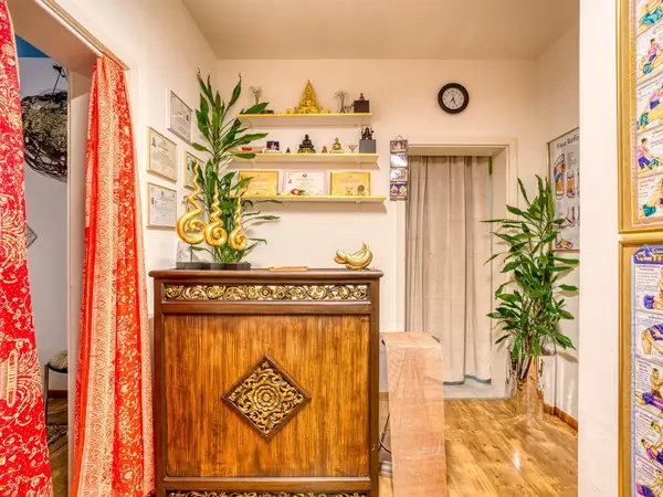 Thai massage reception with wooden counter, plants, certificates, and red curtains