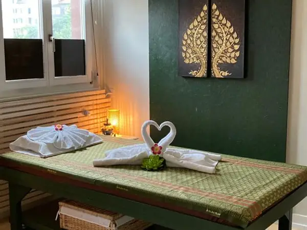 Traditional massage room with green bed, folded towels, and leaf wall art