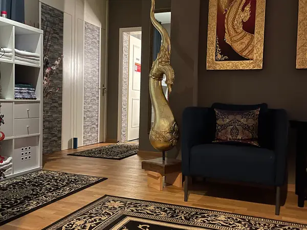 Thai massage waiting area with ornate decor, dark chair, rugs, and open doorway