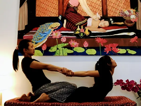 Massage studio with two women stretching beneath Thai-style wall art