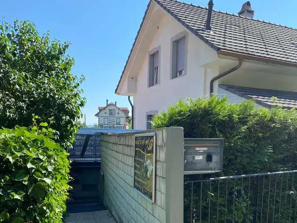 Exterior of a house beside greenery and a low wall under a bright blue sky