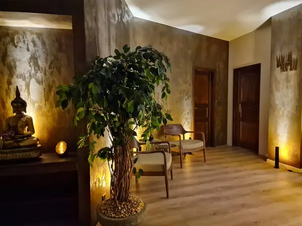 Warm spa waiting area with Buddha statue, potted tree, and wooden chairs