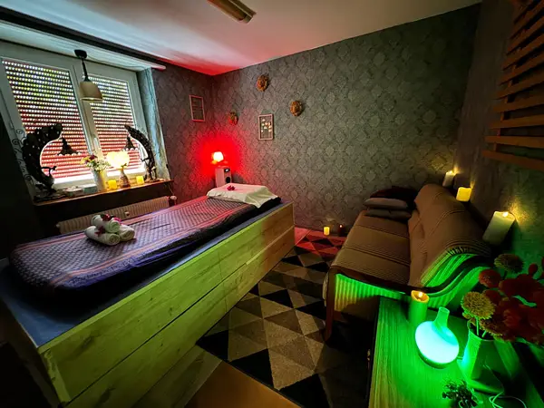 Cozy Thai massage room with treatment bed, sofa, candles, and patterned decor