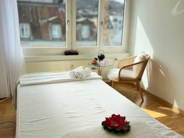 Bright massage room with a treatment bed, chair, and window light