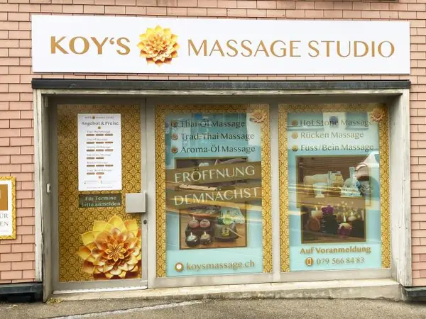 Exterior storefront of Koy’s Massage Studio with gold signage and window posters