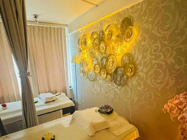 Warm massage room with two treatment beds, beige curtains, and gold wall decor