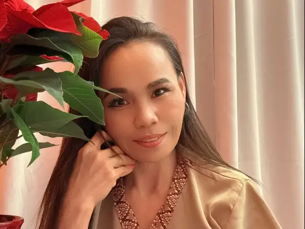 Woman in beige robe beside red flowers and curtains
