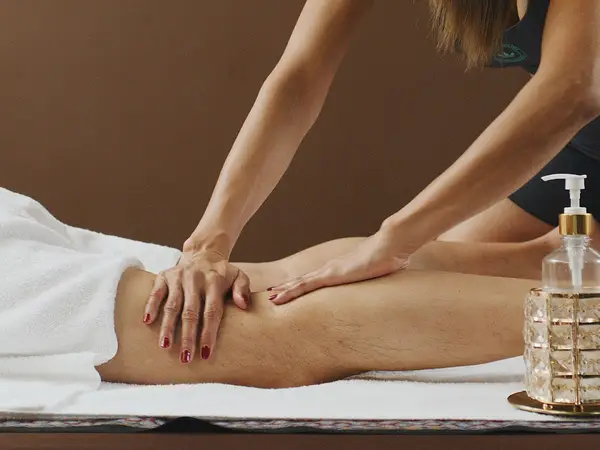 Massage therapist pressing a client’s leg on a treatment table, with lotion bottle nearby