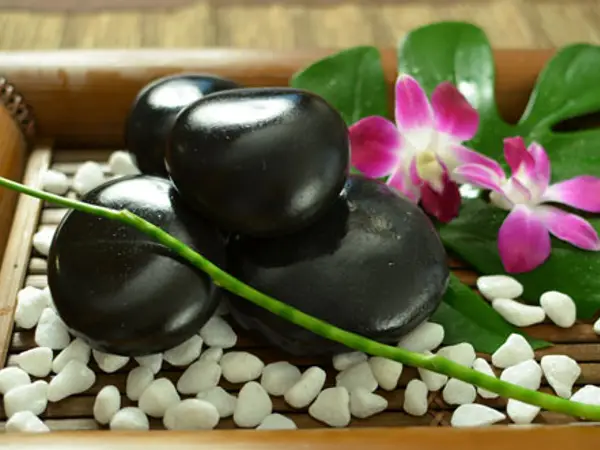 Decorative massage tray with black stones, white pebbles, and pink flowers