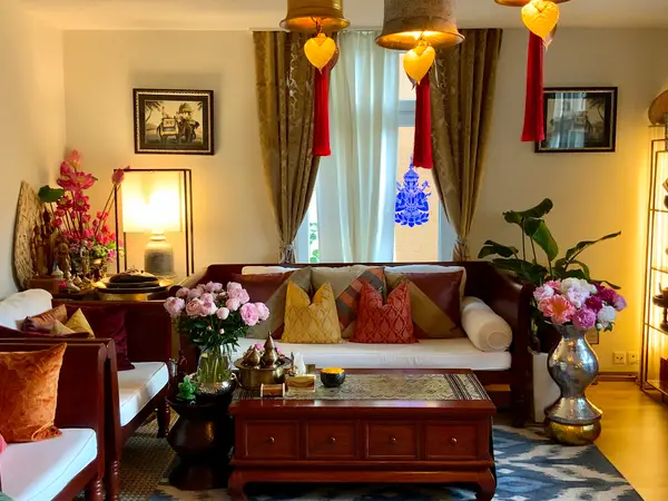 Warm Thai-style lounge with sofas, flowers, lamps, and decorative curtains