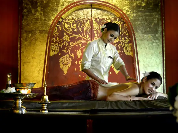 Thai massage room with ornate red-gold decor and a therapist working on a client