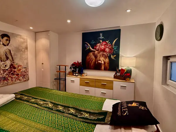 Cozy Thai massage room with green bedspread, wall art, cabinet, and lamp