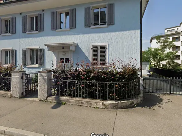 Light blue residential building exterior with black fence and shrubs