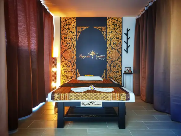 Thai massage room with ornate gold decor, curtained walls, and a centered treatment bed