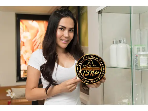 Woman holding a NamPang Thai massage logo in a spa reception area