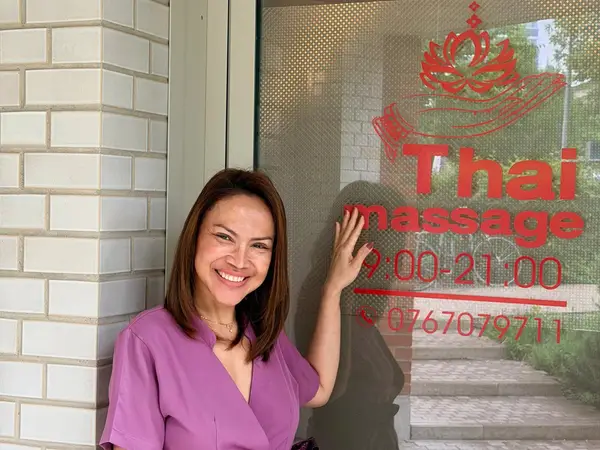 Smiling woman stands beside Thai massage shop window with red signage