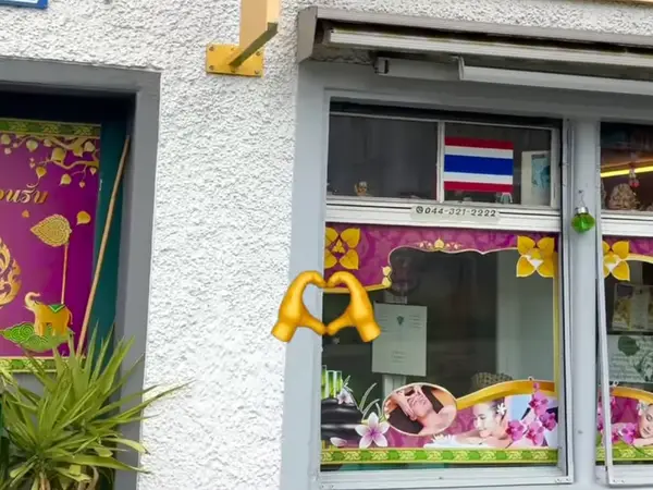 Exterior storefront with Thai flag, colorful window decals, and white stucco wall