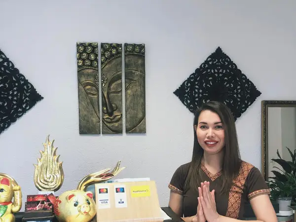 Reception desk with Thai decor and a smiling woman greeting with hands together