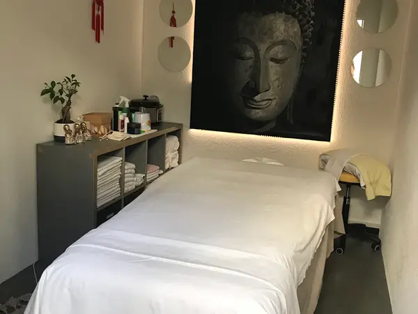 Cozy massage room with a treatment bed, Buddha artwork, and neatly folded towels