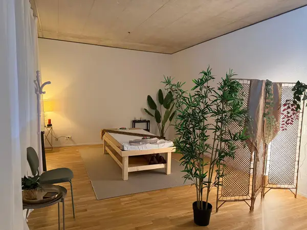 Serene massage room with treatment table, plants, lamp, and folding screens