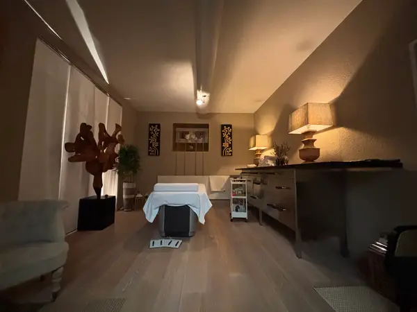 Warm Thai massage room with treatment bed, lamps, and dark wood decor
