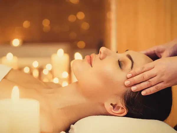 Dim massage room with candles and a woman receiving a head massage
