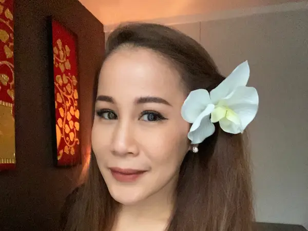 Portrait of a woman with a white flower, warm Thai-style wall decor behind her