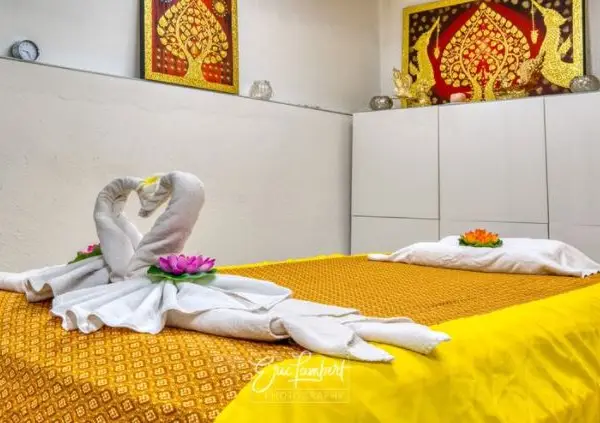 Thai massage room with twin towel swans, yellow bedcover, and ornate wall art