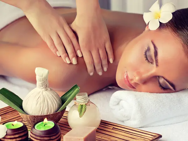 Woman receiving spa massage with candles, oil bottle, and flower on her hair